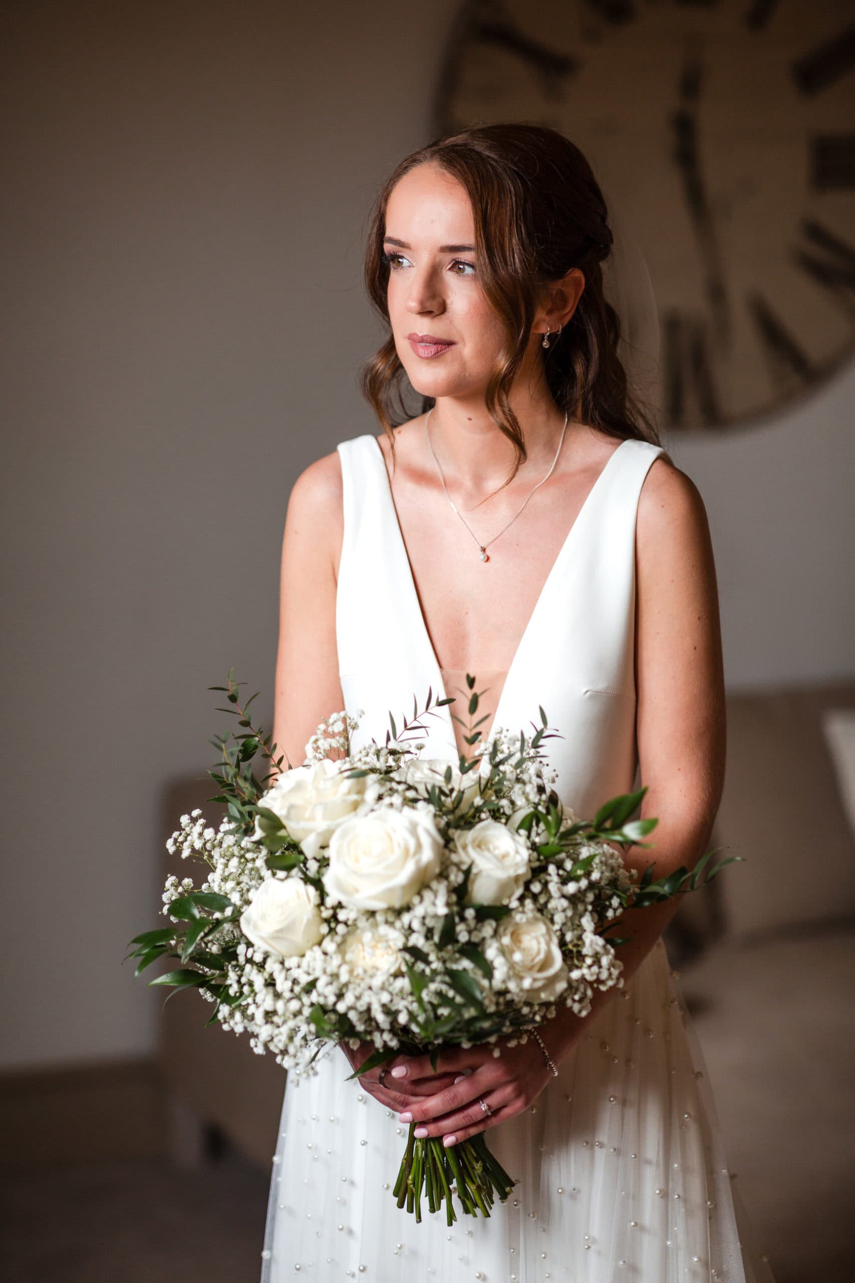 Bride in a plunging neckline holding bouquet of white roses and green foliage