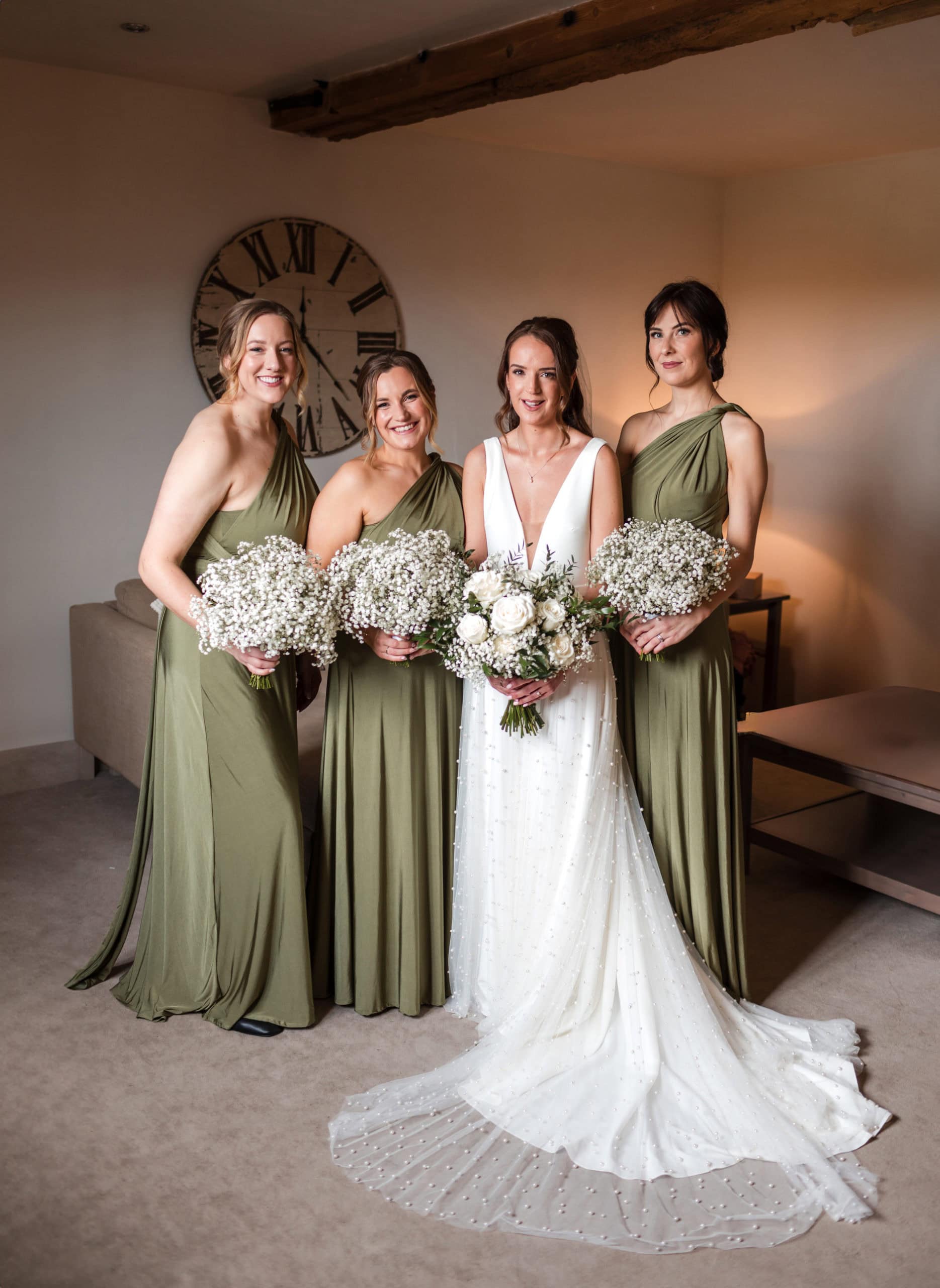 bride wearing Maggie Sottero dress with pearls poses with three bridesmaids in sage green wrap dresses