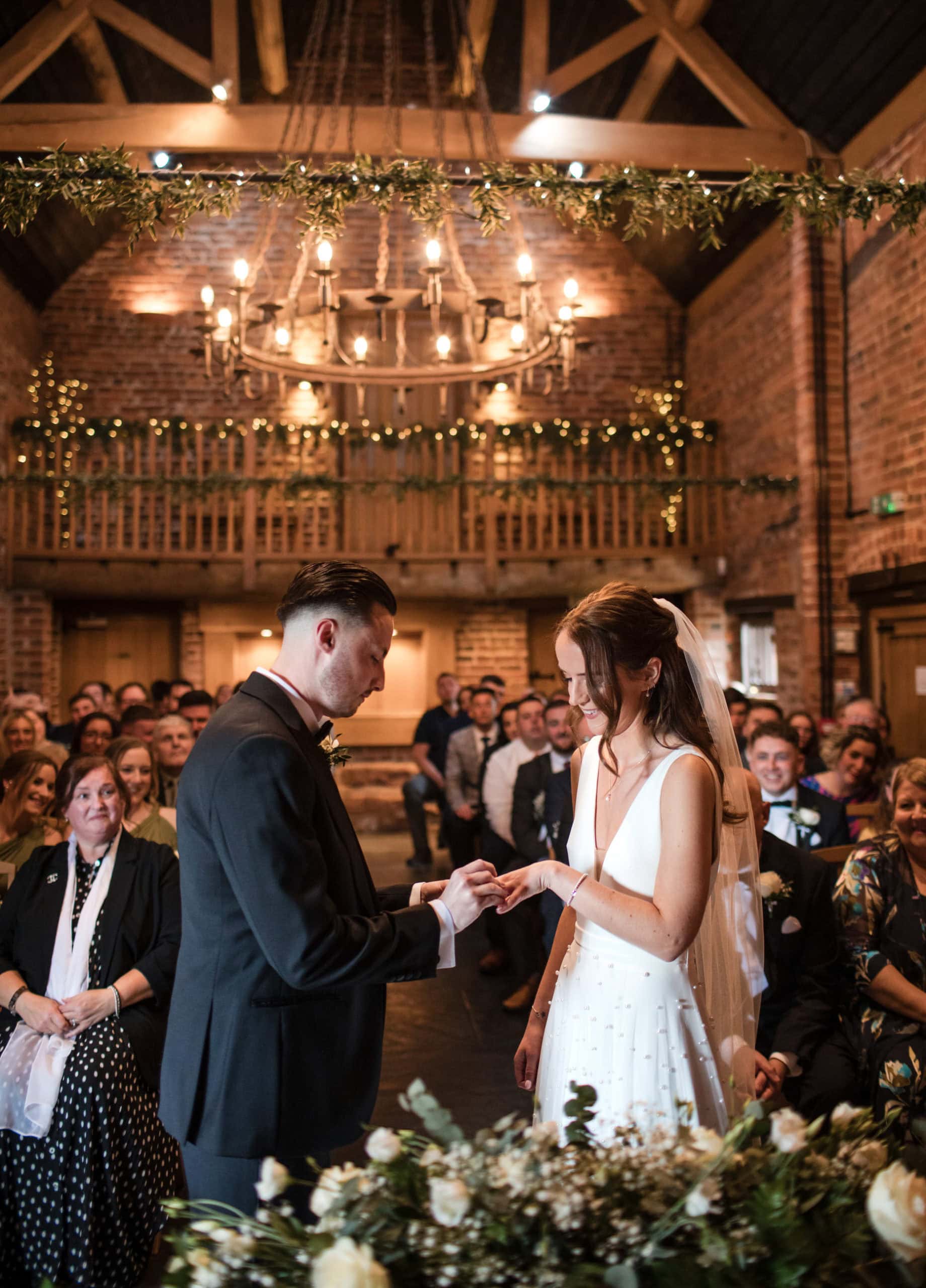 Groom putting ring on Brides finger during their Curradine Barns wedding ceremony