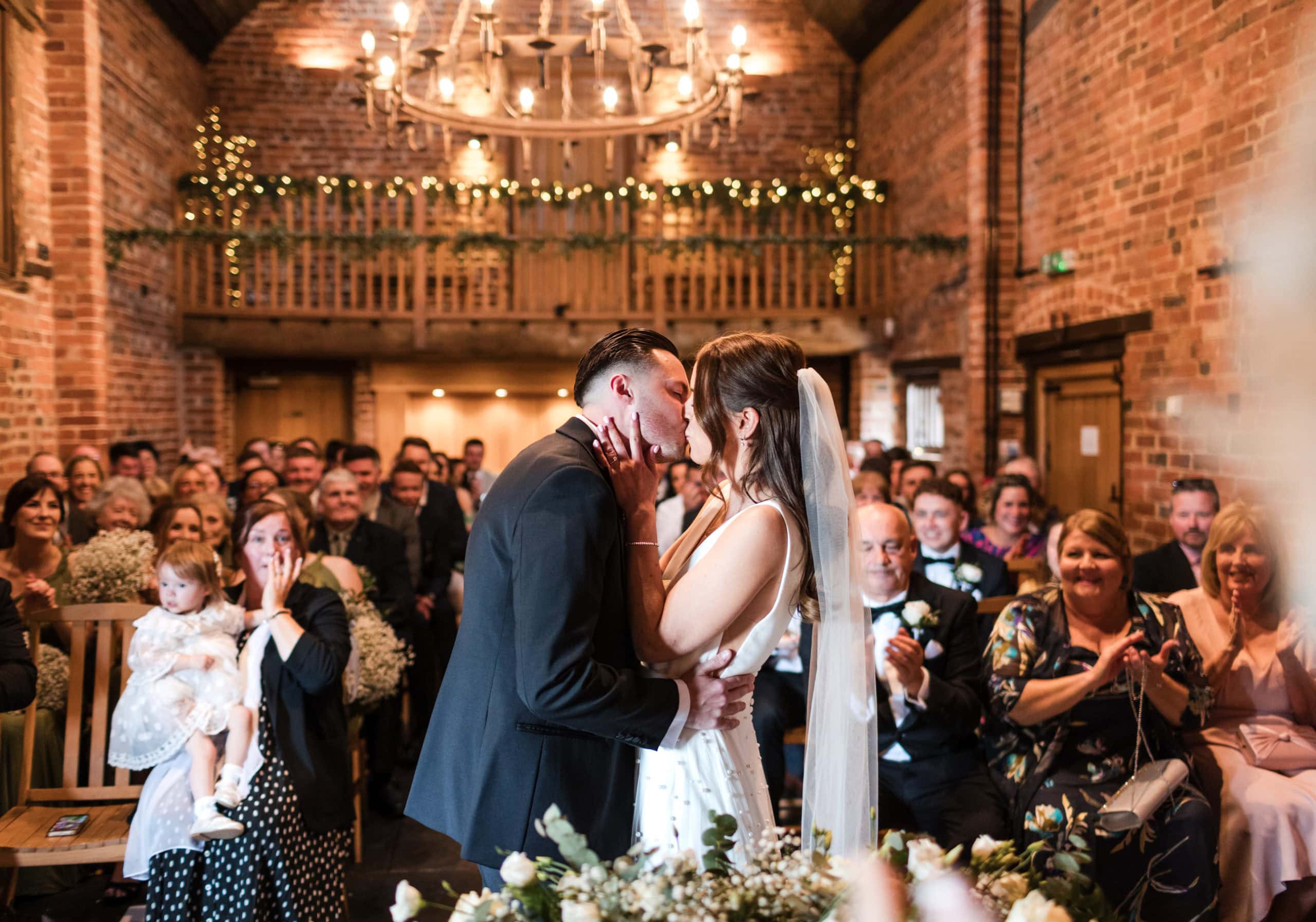 Couple kiss infant of their wedding guests in the Barley Barn