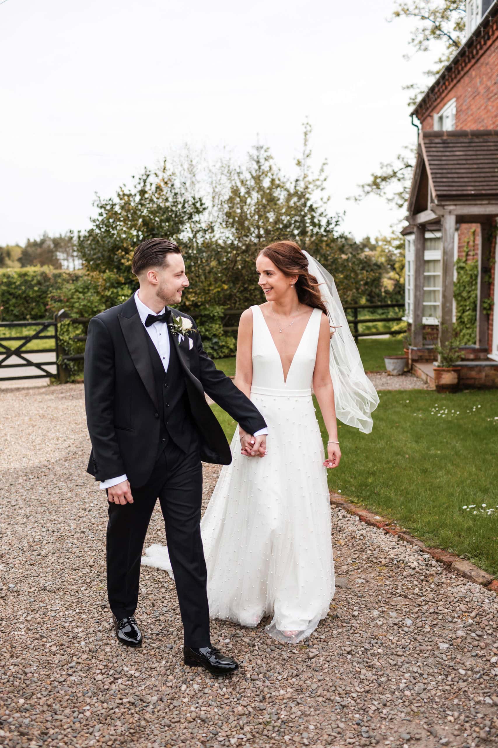 Just married stylish couple walk holding hands in front of the farmhouse at Curradine