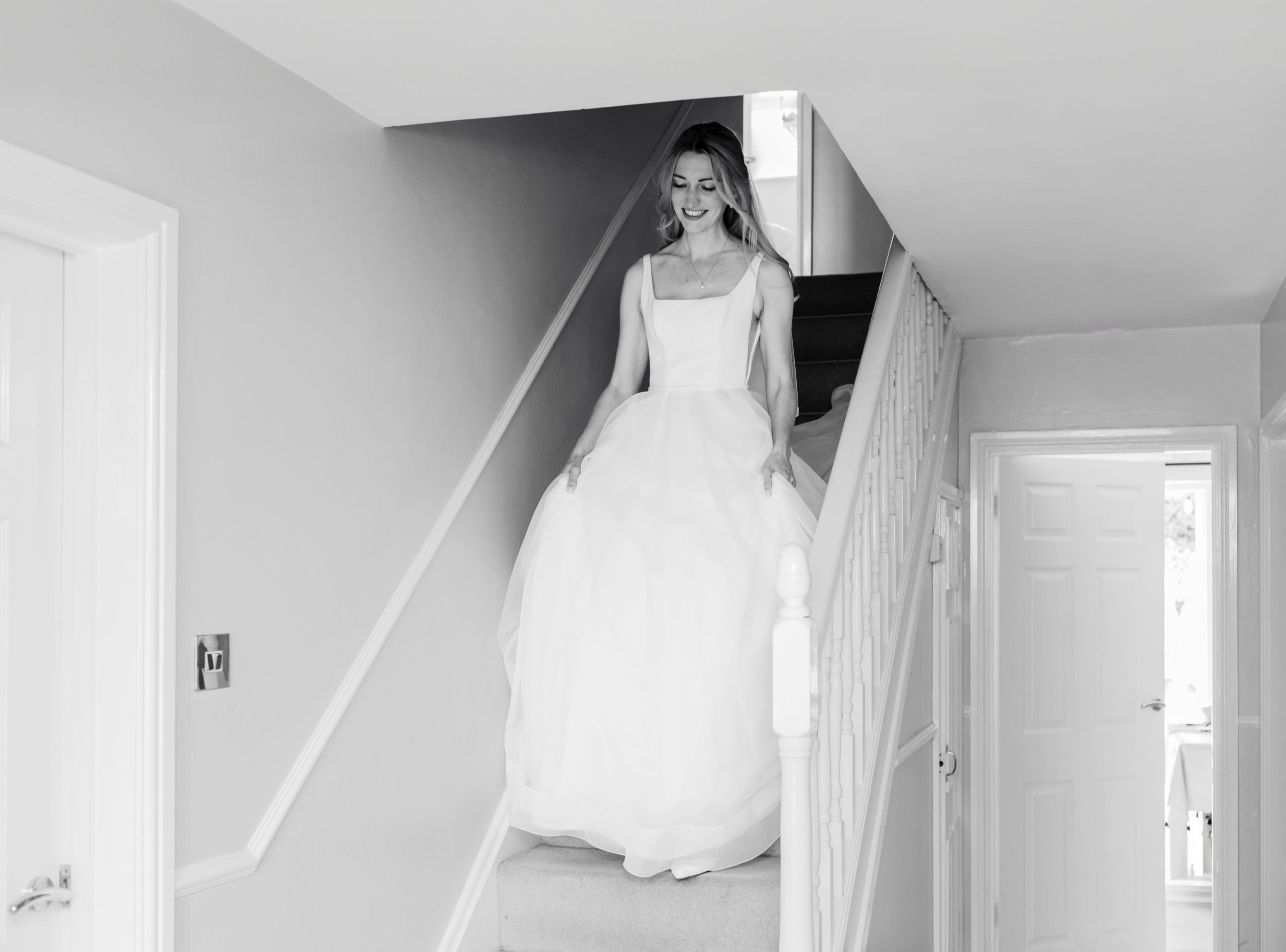 bride walks down stairs at home holding her wedding dress