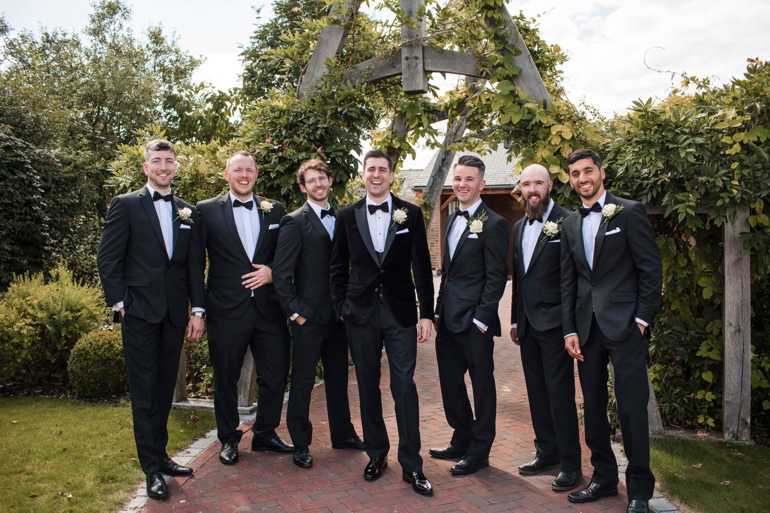 Groom and six Groomsmen wearing black tie stand infant of Wooden Arch 