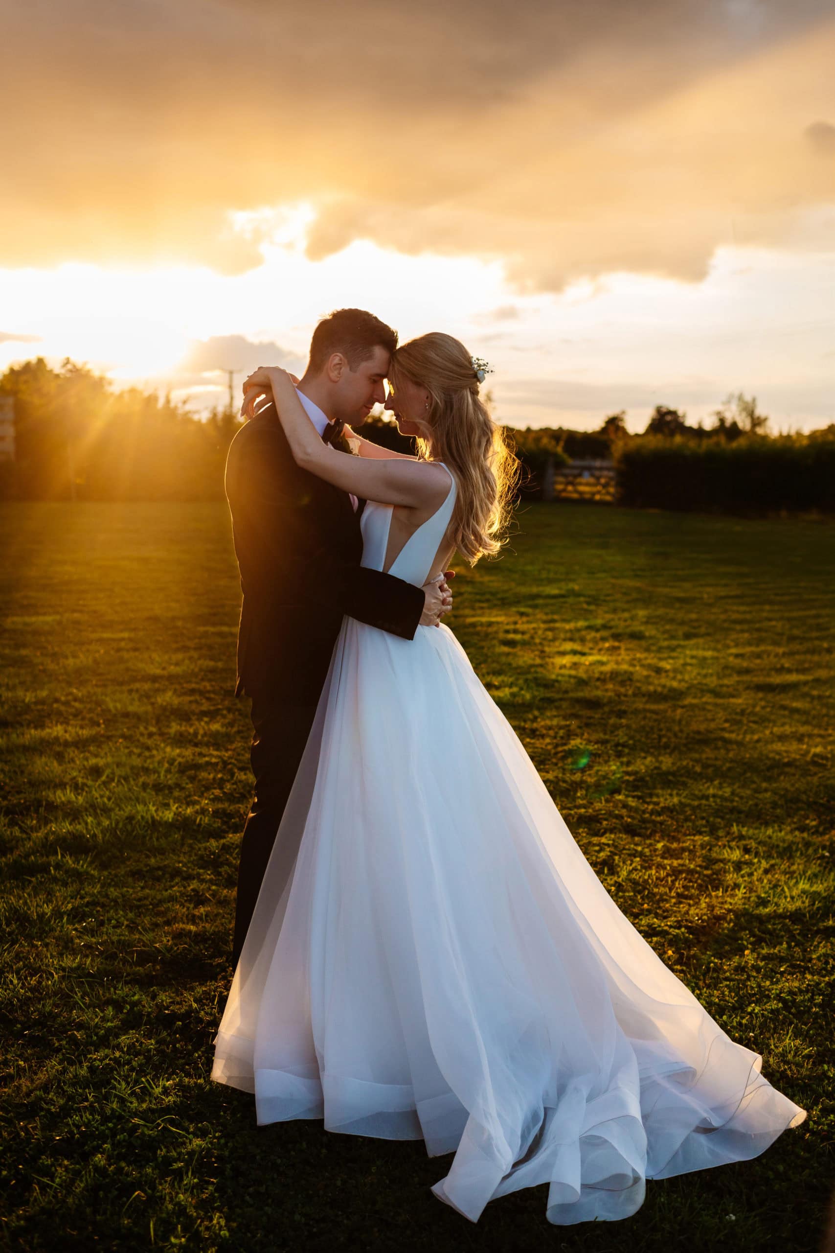 Bride and groom share a hug standing in a field at sunset