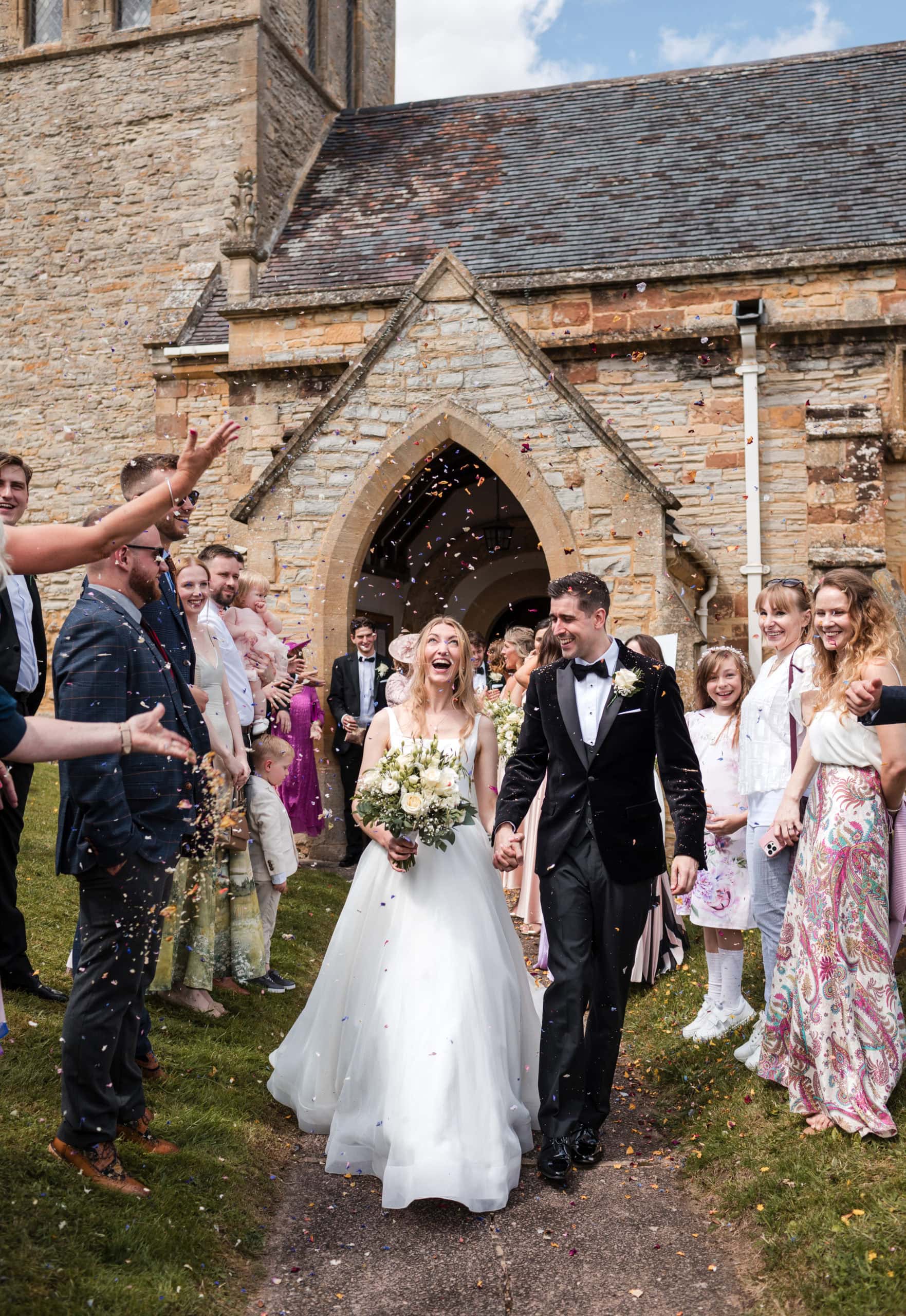 Happy Bride and Groom, walk out of St Peter's Church in Welford on Avon, to confetti