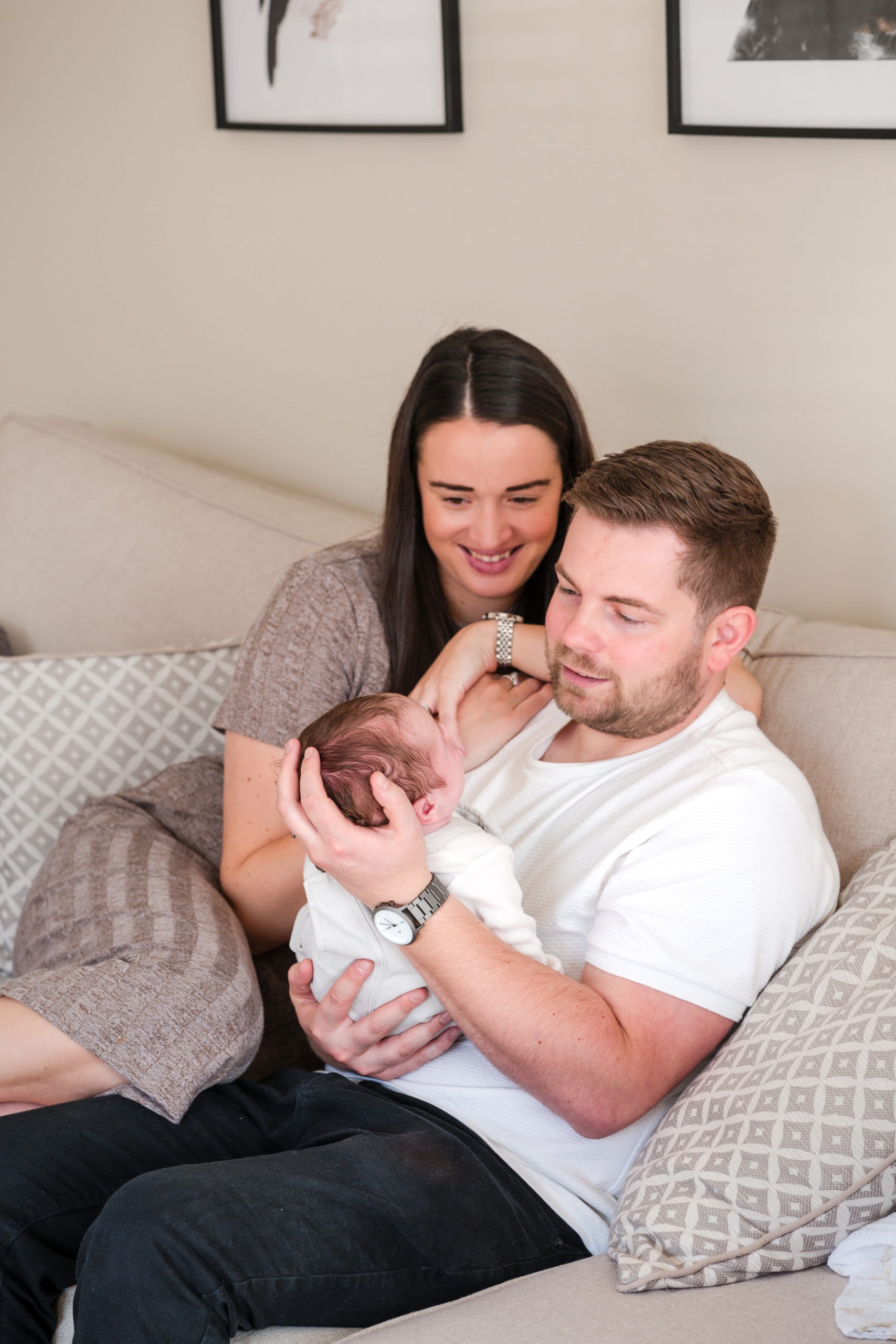 newborn baby is held by his Dad and Mum at home in a neutral coloured living room