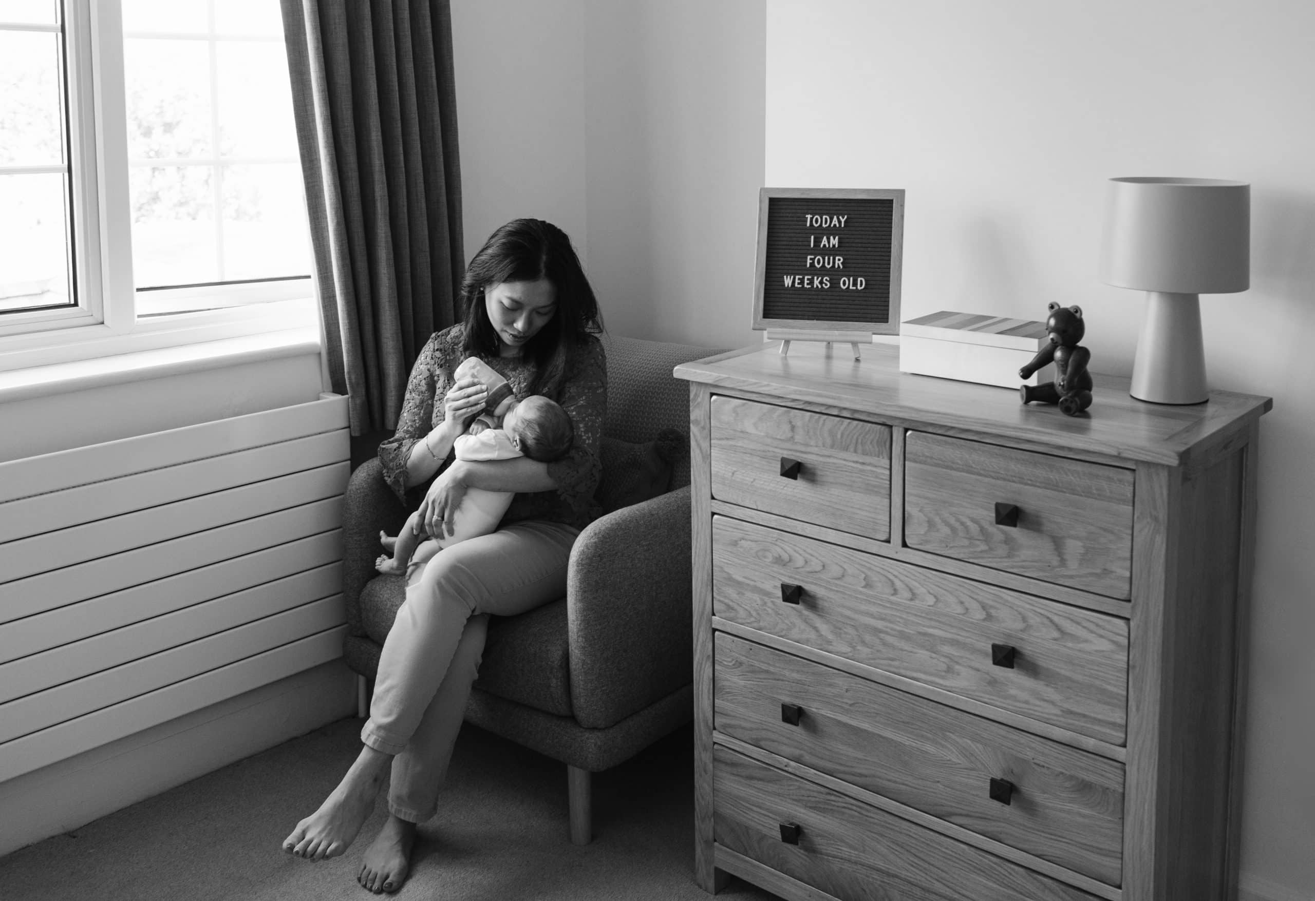 Mum sitting in a chair at home in a nursery feeding her newborn baby