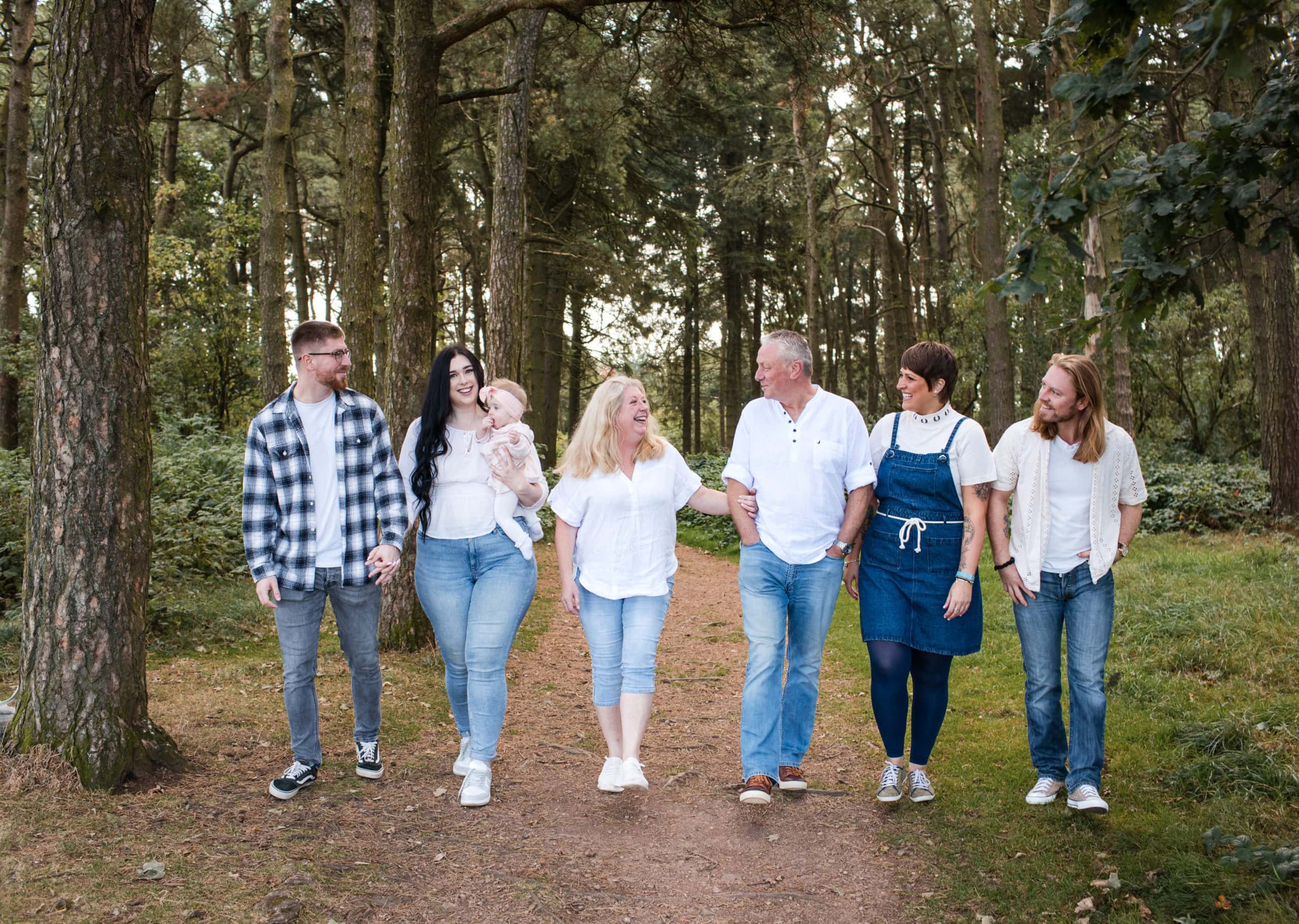 A family of five with grown up children wearing blue demin and white tops, chat and walk together in Lickey Hills Park