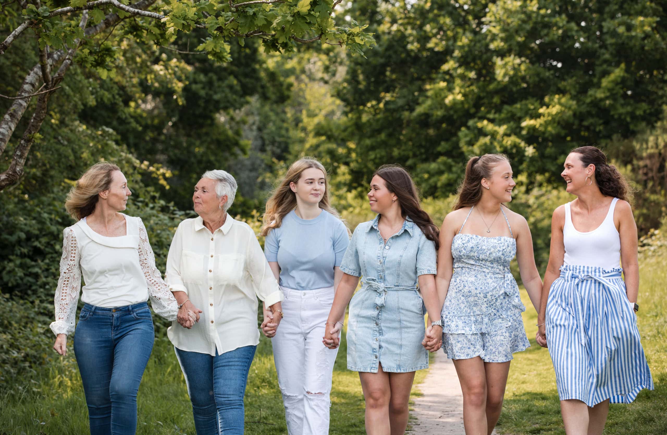 A family group of six women wearing blue hold hands and walk together in Sutton Park